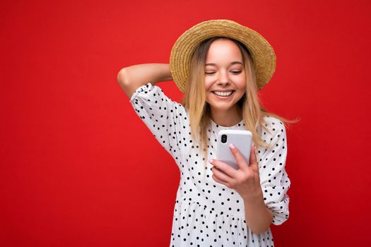 Photo shot of attractive positive good looking young woman wearing casual stylish outfit poising isolated on background with empty space holding in hand and using mobile phone messaging sms looking at smartphone display screen.