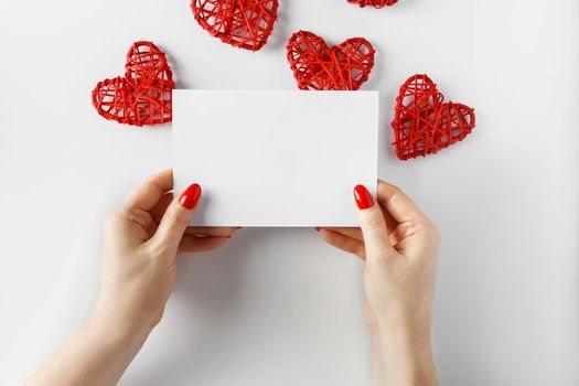 Envelope with a letter in hands on a white background. Blank card in hands on a white background - concept for design. Congratulatory letter on the background of hearts for Valentine's Day.