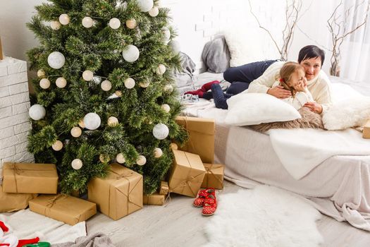 holidays, celebration, family and people concept - happy mother and little girl with gift box over living room and christmas tree background.