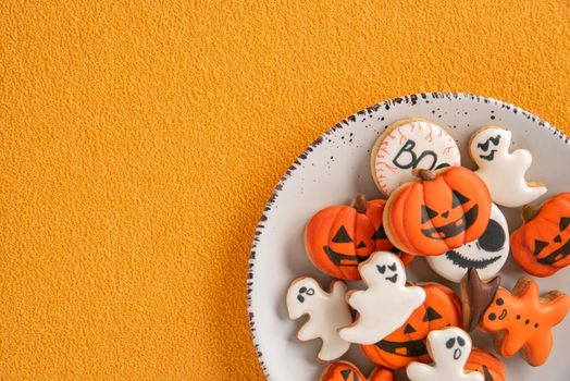 Delicious gingerbread for Halloween in a white plate on an orange background. Pumpkin and ghosts. Background for Halloween with gingerbread. Copy space.