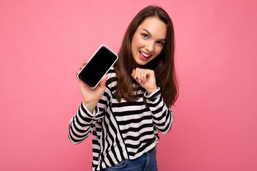 Charming funny adult female person wearing striped sweater isolated over background with copy space looking at camera showing mobile phone screen.