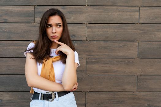 Portrait of touchy sad upset offended resentful young brunet woman wearing casual white t-shirt and jeans with yellow sweater poising near brown wall in the street.