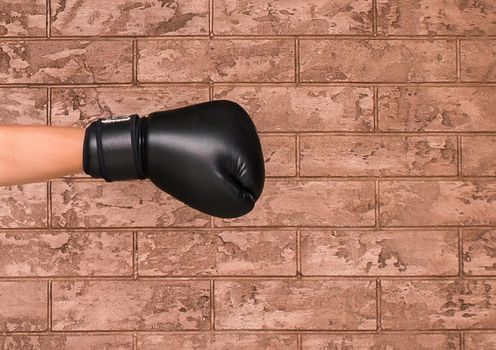 The hand of a guy in a black wrestling glove on a background of a brown brick wall. Boxing concept.