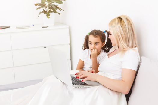 Smiling mother and daughter using laptop in bed at home