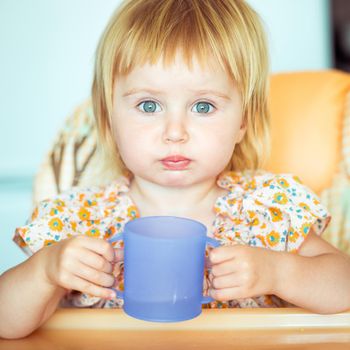 beautiful little girl sitting in a highchair and drinks