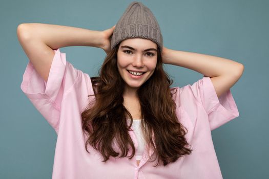 Attractive smiling happy young brunette woman standing isolated over colorful background wall wearing everyday stylish outfit showing facial emotions looking at camera.
