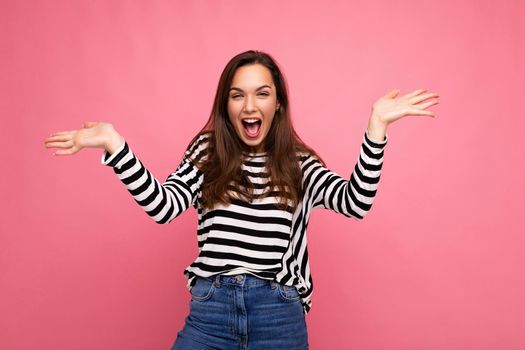 Portrait of young emotional positive shocked surprised happy beautiful brunette woman with sincere emotions in casual striped pullover isolated on pink background with copy space.