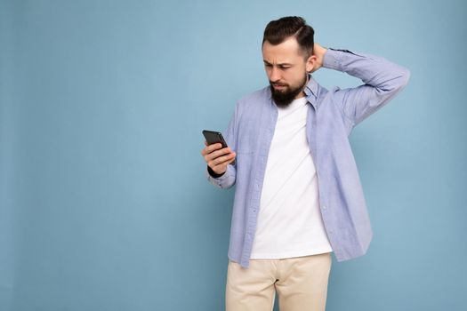 side-profile Photo shot of handsome good looking young man wearing casual stylish outfit poising isolated on background with empty space holding in hand and using mobile phone messaging sms looking at smartphone display screen and thinking over.