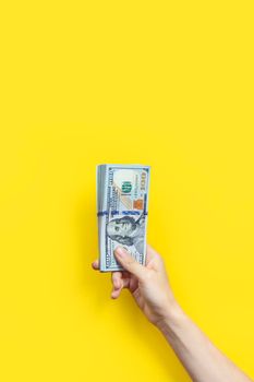 Hand holding a big stack of banknotes isolated on yellow background. Wealth or loan concept. Vertical banner.