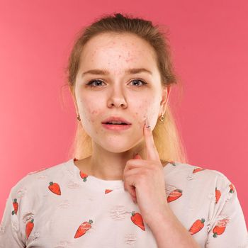 Portrait of teen girl touching her face and looking for acne on ruby background