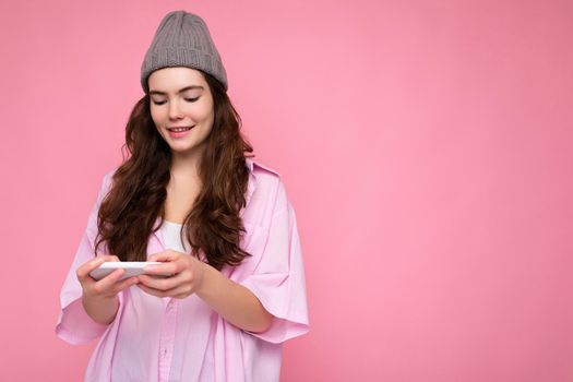 Beautiful young woman wearing casual clothes standing isolated over background surfing on the internet via phone looking at mobile screen.