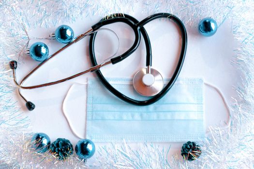 a phonendoscope and a medical mask on a light background with New Year's tinsel and toys. Health care and medicine concept.