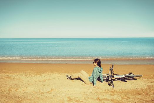 Beautiful young woman resting near a bicycle on beach in summer