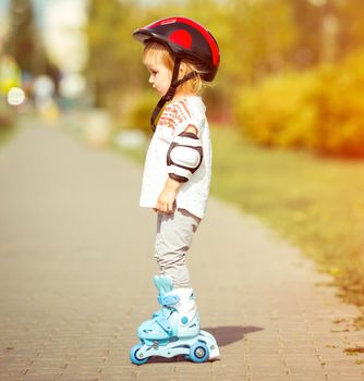 two year old pretty girl in roller skates and a helmet on the street