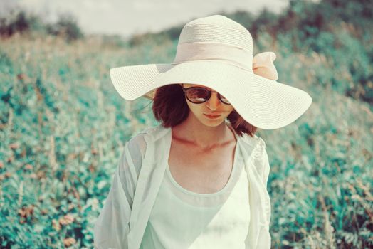 Beautiful fashionable young woman in sunglasses and a hat resting in summer park. Image with instagram color effect