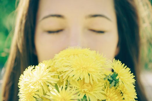 Portrait of beautiful young woman with closed eyes with bouquet of yellow dandelions outdoor in summer, concept of summer mood