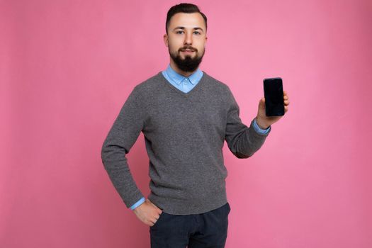 Handsome happy cool young man good looking wearing casual stylish clothes standing isolated over colourful background wall holding smartphone and showing phone with empty screen display looking at camera.