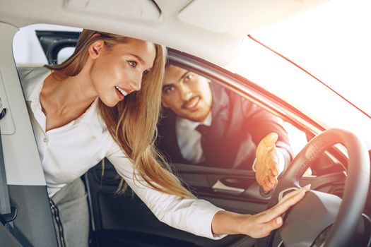 Man car dealer showing a woman buyer a new car in car salon