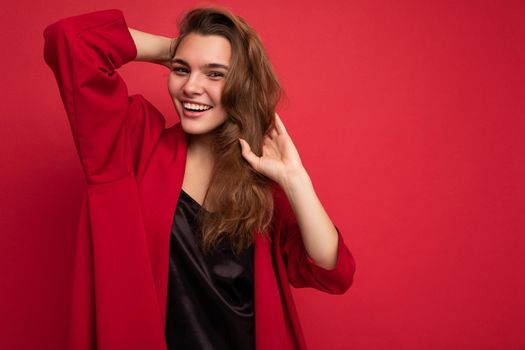 Portrait of positive cheerful fashionable woman in formalwear looking at camera isolated on red background with copy space.