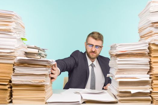 Shocked businessman sitting at the table with many papers in office, he is overloaded with work - image