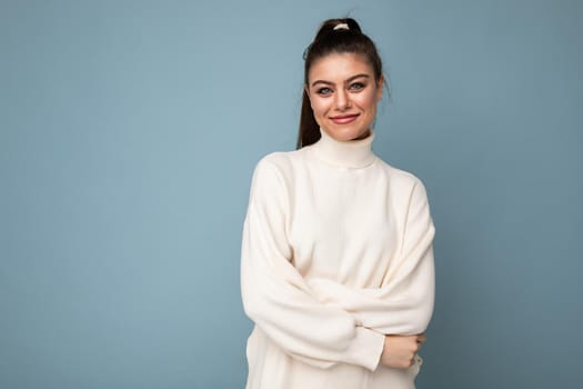 Lovely smiling young woman wearing warm sweater standing isolated over blue background, posing.
