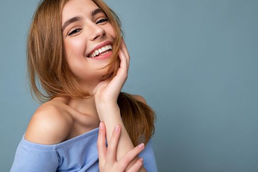 Closeup shot of young happy beautiful dark blonde woman with sincere emotions isolated on background wall with copy space wearing casual blue crop top. Positive concept.