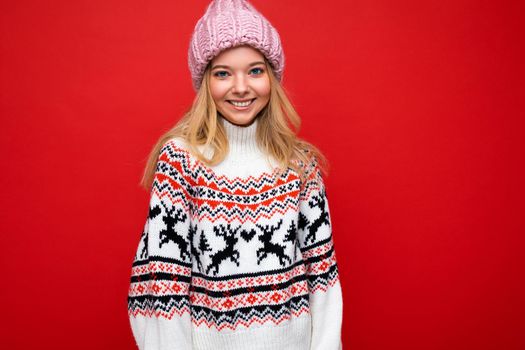 Attractive smiling happy young blonde woman standing isolated over colorful background wall wearing everyday stylish outfit showing facial emotions looking at camera.