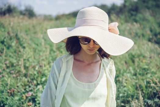 Fashionable young woman in sunglasses and a hat resting in summer park