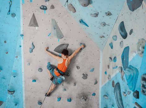 Boy wearing in safety equipment climbing on artificial boulders in gym