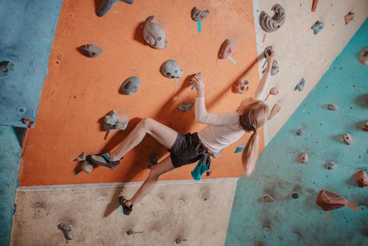 Climber little girl exercises on artificial boulders in gym