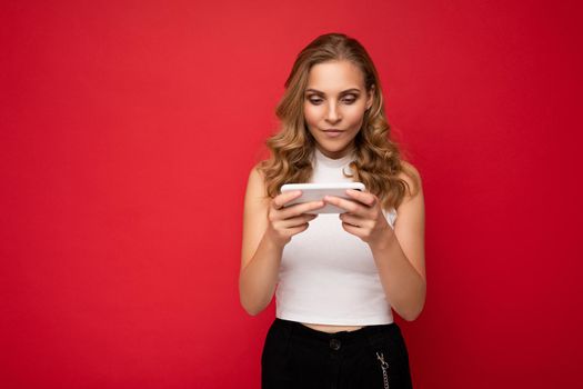 Beautiful young woman wearing casual clothes standing isolated over background surfing on the internet via phone looking at mobile screen.