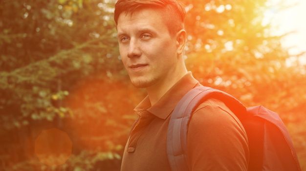 Smiling hiker young man walking in summer forest at sunny day. Image with sunlight effect
