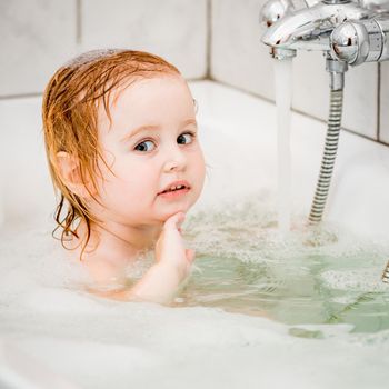 cute two year old baby bathes in a bath with foam closeup