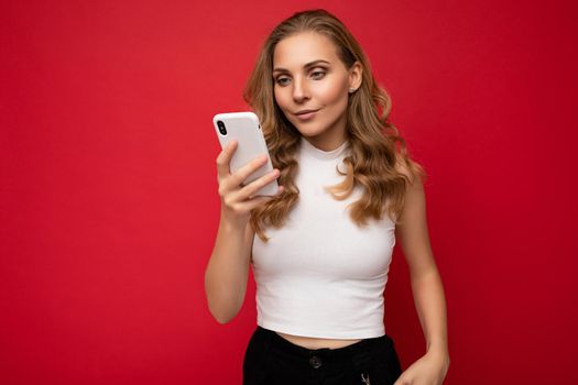 Beautiful young woman wearing casual clothes standing isolated over background surfing on the internet via phone looking at mobile screen.