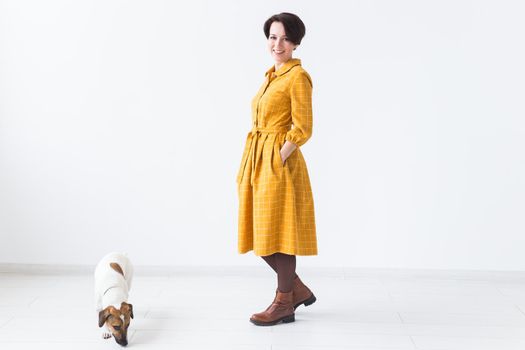 Cheerful young woman posing in a yellow dress with her beloved dog Jack Russell Terrier standing on a white background. The concept of casual wear