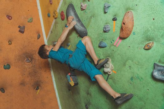 Sporty little boy climbing artificial boulder on practical wall in gym