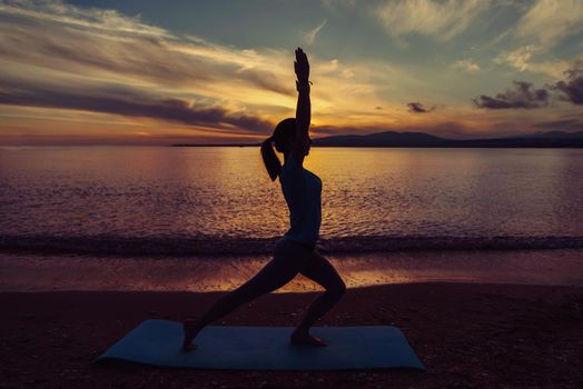 Young woman doing yoga exercise on beach in summer at sunset, concept of healthy lifestyle