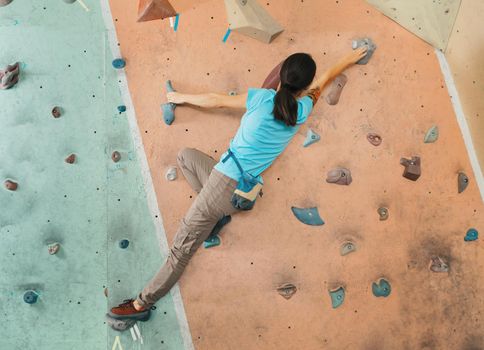 Free climber young woman climbing artificial boulder indoor, bouldering