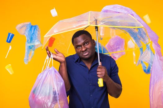 Problem of trash, plastic recycling, pollution and environmental concept - confused man carrying garbage bag on yellow background.