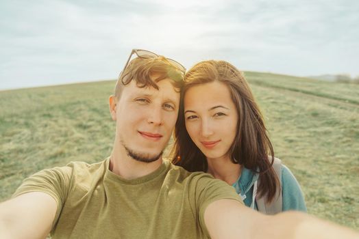 Smiling young loving couple doing selfie in the mountains in summer