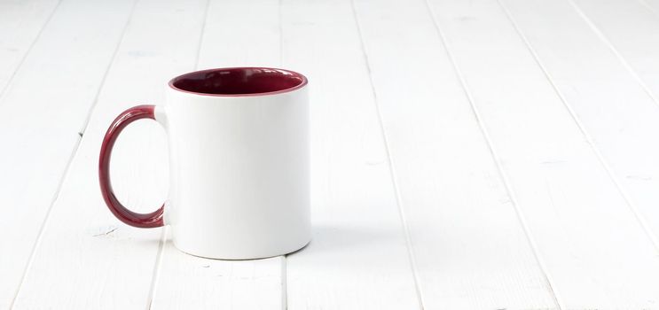 white cup with dark red handle and inside on wooden surface