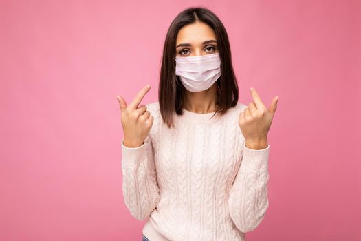 Young beautiful woman in reusable virus protective mask on face against coronavirus isolated on the pink background wall and pointing fingers at yourself.