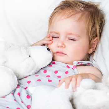 beautiful baby girl with a toys lying in white bed