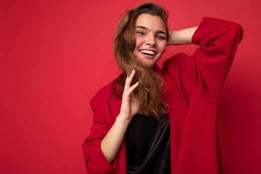 Young beautiful european stylish brunette woman wearing black blouse top and red cardigan isolated over red background with positive sincere emotions. Simple and natural looking at the camera. Free space.