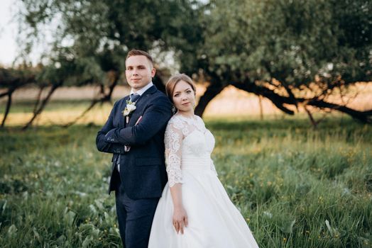 the groom and the bride are walking in the forest near a narrow river on a bright day