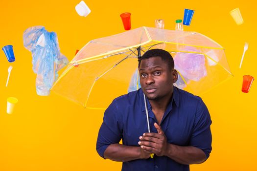 Problem of trash, plastic recycling, pollution and environmental concept - pensive african american man on yellow background with garbage