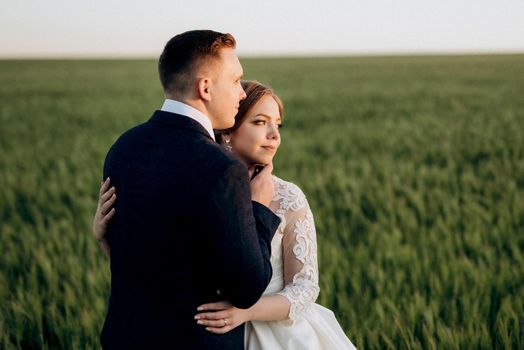 the groom and the bride walk along the wheat green field on a bright day