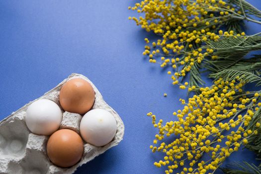 Easter background, eggs and a wooden hare on a blue background, decorated with Mimosa flowers, flatlay, top view, empty space for text. happy Easter.