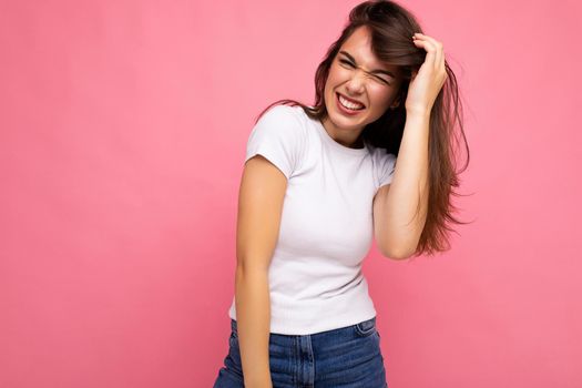 Photo portrait of young beautiful smiling hipster brunette woman in white t-shirt with mockup. Sexy carefree female person posing isolated near pink wall with empty space in studio. Positive model with natural makeup.