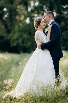 the groom and the bride are walking in the forest near a narrow river on a bright day